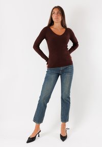 Top lungo a maniche ribbed di colore marrone con scollatura a V, abbinato a jeans a gamba dritta blu e tacchi a punta neri.