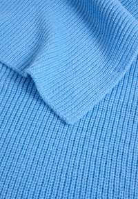 Tessuto lavorato a maglia di colore blu chiaro con una texture a costine, caratterizzato da un bordo ripiegato, che mostra un aspetto morbido e accogliente con un motivo uniforme.