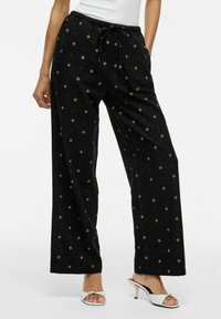 Pantaloni larghi neri con vita regolabile, caratterizzati da un motivo a diamante e sottili accenti argentati. Realizzati in morbido tessuto testurizzato.