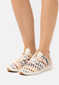 Flerfärgad sneaker med ett mönstrat textilöverdrag som har orange, svart och gula rutor; vit sula och tanaccent.