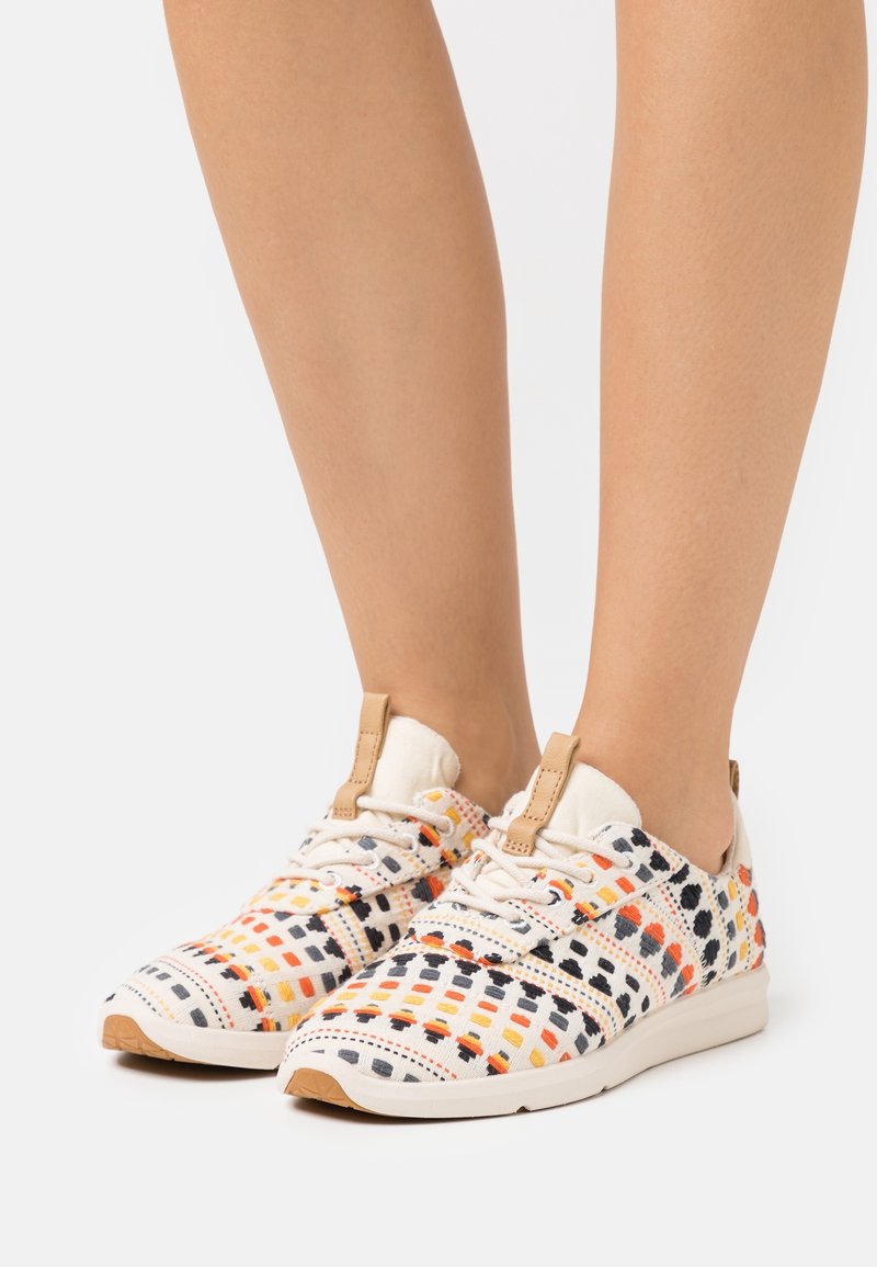 Flerfärgad sneaker med ett mönstrat textilöverdrag som har orange, svart och gula rutor; vit sula och tanaccent.