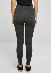Leggings noirs taille haute avec un motif pied-de-poule texturé et une coupe longueur cheville, associés à des chaussures noires sans lacets.