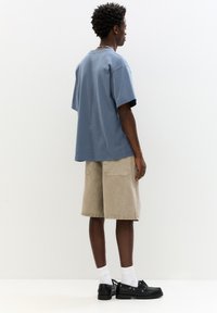 Bequemes, hellblaues Baumwoll-T-Shirt mit Rundhalsausschnitt, kombiniert mit beigen Cordshorts mit zwei Gesäßtaschen und schwarzen Schuhen.
