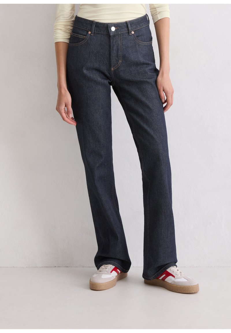 Dunkelblaue Denim-Jeans mit geradem Bein, ausgestattet mit kupferfarbenen Nähten, einem Knopfverschluss vorne und fünf Taschen. Kombiniert mit lässigen Sneakers.