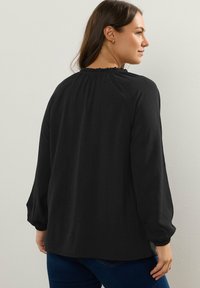 Blusa nera a maniche lunghe con scollatura arricciata e tessuto texture. Presenta polsini elasticizzati e una vestibilità rilassata.
