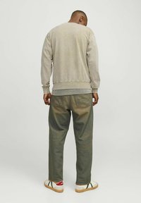 Sudadera beige con cuello redondo y puños acanalados, combinada con jeans verde oscuro que presentan un leve degradado y zapatillas blancas con acentos verdes.