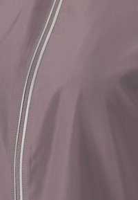 Let fyrig, mauve jakke med lynlås foran i grå nuancer og en glat, let shiny tekstur.