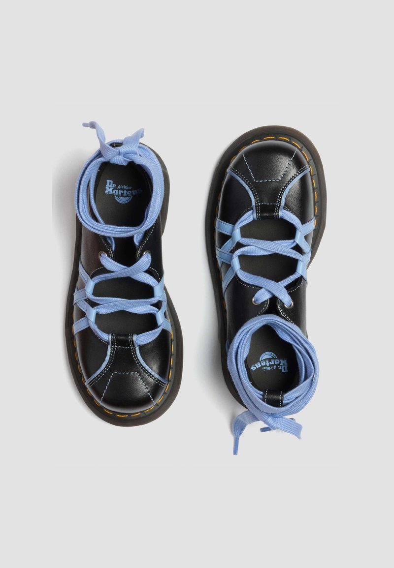 Black leather Dr. Martens shoes with light blue crisscross laces and yellow stitch detail around the sole, shown from above on a white background.