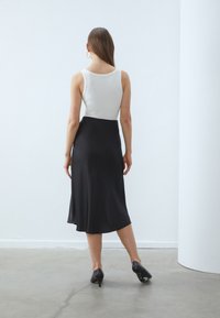 Ærmeløs hvid top og sort midi-nederdel; glat stof med en let glans; tætsiddende silhuet; simpel design; båret med sorte hæle.