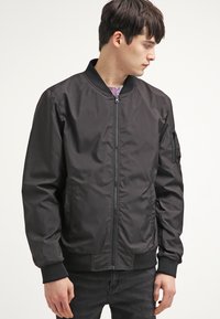 Musthave mustang-jope, millel on lukuga kinnis ja ribikätised. Küljetasku ja valmistatud sileda, kergest kangast. Minimalistlik disain.