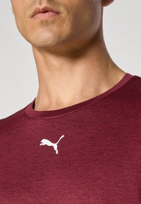 Bordeauxrotes Sport-T-Shirt mit Rundhalsausschnitt, aus strukturiertem Stoff. Mit einem weißen Puma-Logo auf der oberen linken Brustseite.