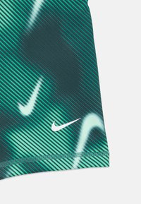 Sezione di tessuto a strisce verdi e nere con il logo Nike swoosh bianco e cuciture visibili lungo il bordo.