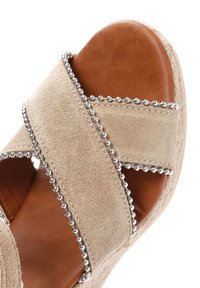 Beige suède wedge sandaal met gekruiste banden, zilveren kraalaccenten en een bruin lederen inleg. Gegoten zool voor grip.