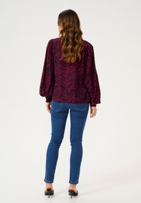 Halenka s dlouhými rukávy s černo-fuchsiovým zebra potiskem, s volánkovými rukávy; kombinováno s úzkými modrými džíny a černými lodičkami.
