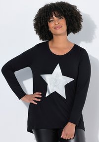 Zwarte langemouwen top met een groot zilveren sterontwerp en een gestructureerd patroon. De stof lijkt zacht en iets getailleerd bij de taille.
