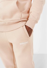 Perzikkleurige sweatshirt met geribbelde manchetten en zoom, voorzien van een voorzak. Vergezeld van bijpassende sweatpants met witte logo detail.