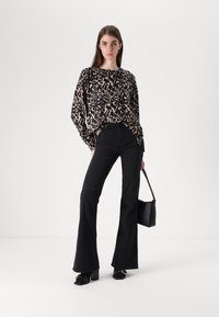 Black and tan patterned long-sleeve top paired with high-waisted black flared jeans. Black handbag and block-heeled shoes complete the look.