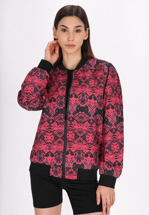 Giacca bomber rossa e nera con motivi geometrici, polsini e vita a costine. Chiusura con zip nera, tessuto leggero con una finitura liscia.
