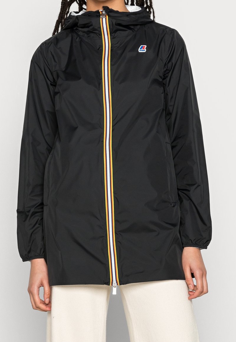 Schwarze Regenjacke mit Kapuze, ausgestattet mit einem Frontreißverschluss, der mit gelben, weißen und roten Streifen verziert ist. Elastische Bündchen und lockerer Schnitt.