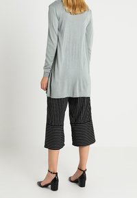Světle šedé tričko s dlouhým rukávem a volným střihem, doplněné černobílými pruhovanými culoty. Černé boty na podpatku dokončují outfit.