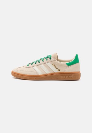 Beżowe buty sportowe Adidas Spezial z zieloną zakładką na pięcie i sznurowadłami, białe trzy paski, gumowa podeszwa oraz złote logo "Spezial" po boku.