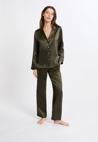 Conjunto de pijama de raso verde oliva, que incluye una camisa abotonada de manga larga y pantalones de pierna recta con textura suave y detalles mínimos.