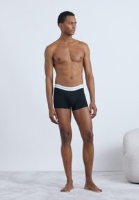 Boxer aderenti neri con una cintura bianca, realizzati in un tessuto morbido. Il design è aderente e la superficie appare liscia e stretch.