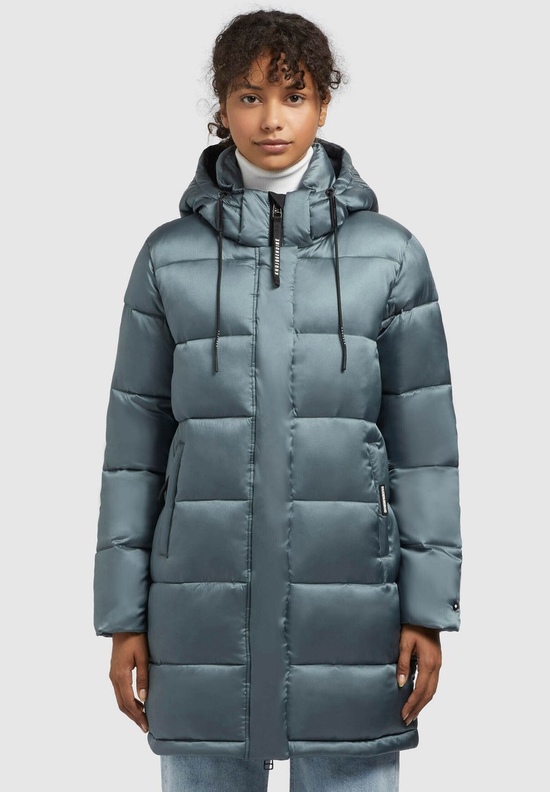 Parka căptușit în culoare teal cu un finisaj lucios, glugă ajustabilă, fermoar frontal și buzunare laterale; prezintă o formă pătrată și un design matlasat.