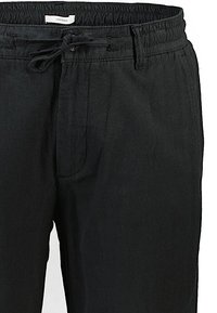 Zwarte linnenmix broek met een elastische tailleband, trekkingdetail en een voorzak. De stof heeft een soepele textuur en een relaxte pasvorm.
