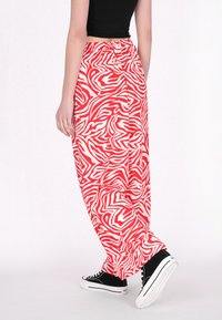 Rood en wit gestreepte broek met losse pasvorm en elastische tailleband, gecombineerd met zwarte hoge sneakers op een lichte achtergrond.