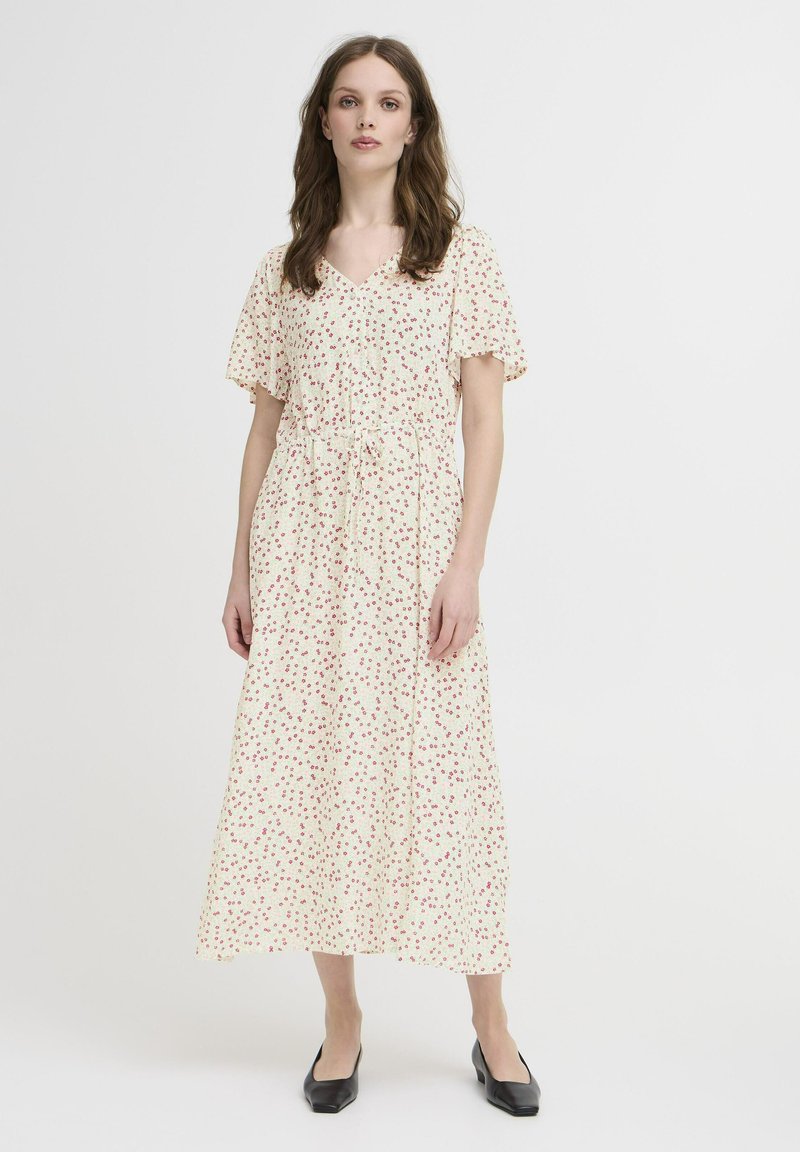 Floral midi-kjole i cremefarve med små røde og grønne mønstre, v-hals, korte flæseærmer og snøre i taljen. Bruget med sorte ballerinasko.
