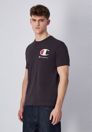 Camiseta de algodón negra con cuello redondo. Presenta un logotipo de Champion en rojo y blanco en el lado izquierdo del pecho. Mangas cortas, diseño ligeramente ajustado.