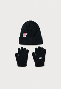 Fekete kötött sapka animált piros címkével és fekete kötött kesztyűkkel, az egyiken fehér Nike logó látható, fehér háttéren elhelyezve.