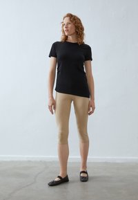 T-shirt nera aderente, leggings beige e ballerine nere. La maglietta ha maniche corte; i leggings sono alla caviglia, in tessuto liscio; le ballerine hanno una punta rotonda.