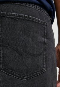 Jeans en denim gris foncé avec une poche arrière ornée d'un motif de couture discret. La texture du matériau est caractéristique du denim standard.