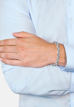 Silver chain bracelet with interlocking links, worn on a wrist with light skin. Hand resting on a light blue shirt sleeve.