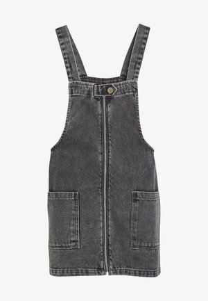Zwart gewassen denim salopetjurk met rits aan de voorkant, twee vierkante voorzakken, verstelbare schouderbanden en een drukknop bij de halslijn.