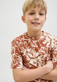 Camiseta infantil de manga corta en color óxido con un patrón floral tropical blanco, cuello redondo y textura suave.