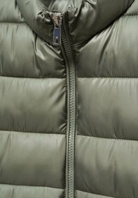 Oliwkowa kamizelka puchowa z wysokim kołnierzem, pikowanym wzorem i centralnym zamkiem błyskawicznym z metalowym uchwytem. Miękka, gładka tekstura.