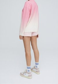 Vaaleanpunainen liukuvärjätty pitkähihainen paita, joka muuttuu valkoiseksi, yhdistettynä vaaleanpunaisiin shortseihin ja valkoisiin lenkkareihin, joissa on vaaleanpunaisia yksityiskohtia sekä siniraitaiset sukat.