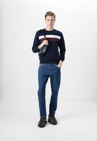 Navy sweatshirt med hvite og burgunder striper, blå jeans og svarte sneakers. Liten crossover-veske i svart henger på venstre skulder.