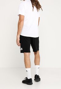 Camiseta atlética blanca, pantalones cortos negros con el logo blanco de "adidas", zapatos negros y calcetines blancos. Diseño simple, tejido ligero.