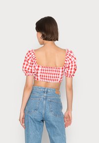 Top curto em xadrez vermelho e branco com mangas bufantes e decote quadrado, combinado com jeans de ganga azul de cintura alta.