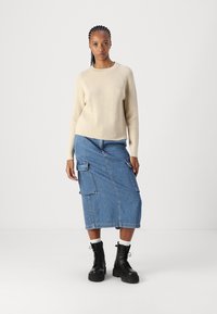 Μπεζ ριμπ πλεκτό πουλόβερ σε συνδυασμό με μπλε τζιν μίντι φούστα που διαθέτει δύο πλάγιες τσέπες και μαύρα στρατιωτικά μποτάκια με χοντρούς πάτους.