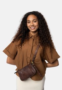 Borsa a tracolla in pelle marrone con una texture liscia e una chiusura con zip, dotata di un cinturino rimovibile e di sottili dettagli in metallo.
