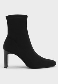 Svart ankelstrumpa med spetsig tå och smal hög klack, med slät tyg och sömdetaljer på sidan.