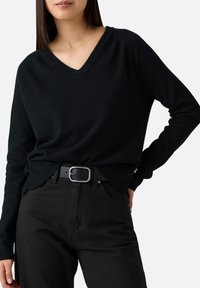 Maglione nero a scollo a V realizzato in tessuto morbido, con maniche lunghe e un fit rilassato, abbinato a jeans neri e una cintura con fibbia argentata.