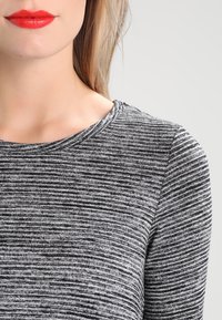 Top a righe grigie e nere con scollatura rotonda, realizzato in tessuto morbido. Inquadratura ravvicinata che enfatizza la texture e i dettagli del motivo.