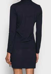 Mörkblå långärmad klänning, smal passform, mjuk tyg, midjekorts längd, med sidofläktar vid fållen, enkel kragsdesign.