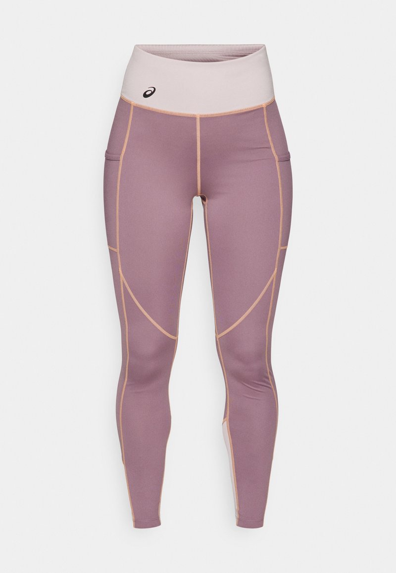 Leggings en tissu lisse et extensible de couleur violet clair avec des accents beiges. Ils présentent une taille haute et des poches latérales.
